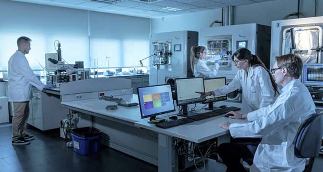 A team of scientists in lab coats working diligently on computers in a research laboratory.