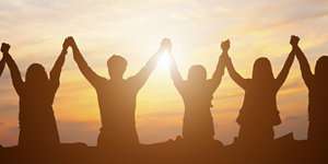 Silhouette of people raising hands at sunset, expressing joy and unity in a beautiful outdoor setting.